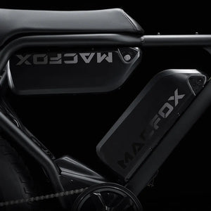 Side view of the Macfox X2 eBike in a rugged outdoor setting, showcasing its sturdy frame, fat tires, and front suspension fork.