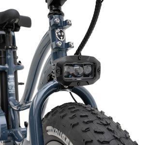 A black Murf Higgs Plus eBike parked on a paved path, featuring fat tires, a step-through frame, and a rear cargo rack, with greenery in the background.