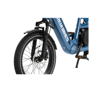 A silver eBike Revi Flux ST parked on a paved path, featuring a step-through frame, front suspension fork, and rear rack, with trees and greenery in the background.