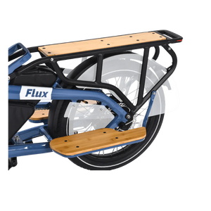 A silver eBike Revi Flux ST parked on a paved path, featuring a step-through frame, front suspension fork, and rear rack, with trees and greenery in the background.