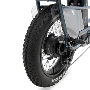 A black Murf Higgs Plus eBike parked on a paved path, featuring fat tires, a sturdy frame, and a rear cargo rack, with greenery in the background.