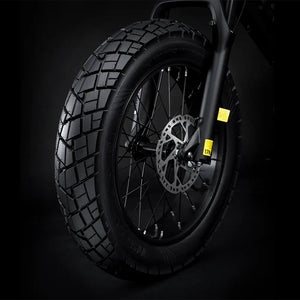 Electric bike Macfox X7 in matte black, shown from a side angle with thick tires, front suspension fork, and a sturdy frame, displayed outdoors on a paved path.