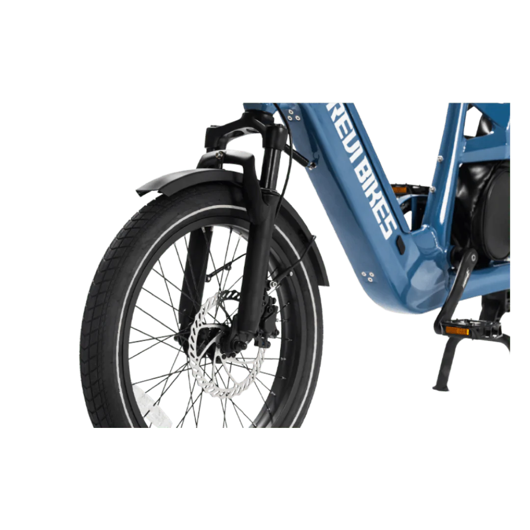 A silver eBike Revi Flux ST parked on a paved path, featuring a step-through frame, front suspension fork, and rear rack, with trees and greenery in the background.