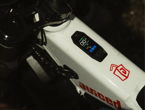 Juiced Scrambler electric bike side view, black frame, fat tires, long padded seat, and retro-style headlight on a white background.