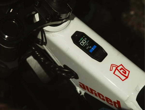 Juiced Scrambler electric bike side view, black frame, fat tires, long padded seat, and retro-style headlight on a white background.