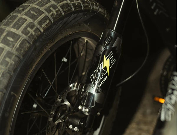 Electric bike parked outdoors, featuring a retro motorcycle-inspired design with a long seat, wide tires, and a matte black frame.