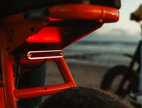 Electric bike parked outdoors, featuring a retro-inspired design with fat tires, a long padded seat, and a matte black frame.
