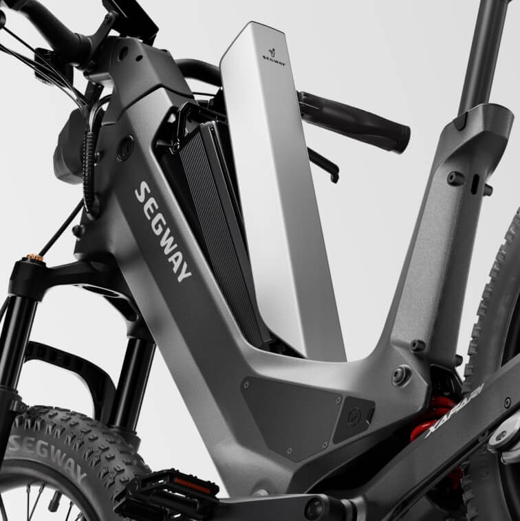A Segway Xafari eBike parked outdoors on a gravel path, surrounded by greenery, showcasing its sturdy frame, wide tires, and integrated battery.