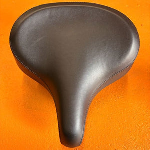 A black eBike seat in a beach cruiser style with a wide, cushioned design and visible stitching, shown against a plain white background.
