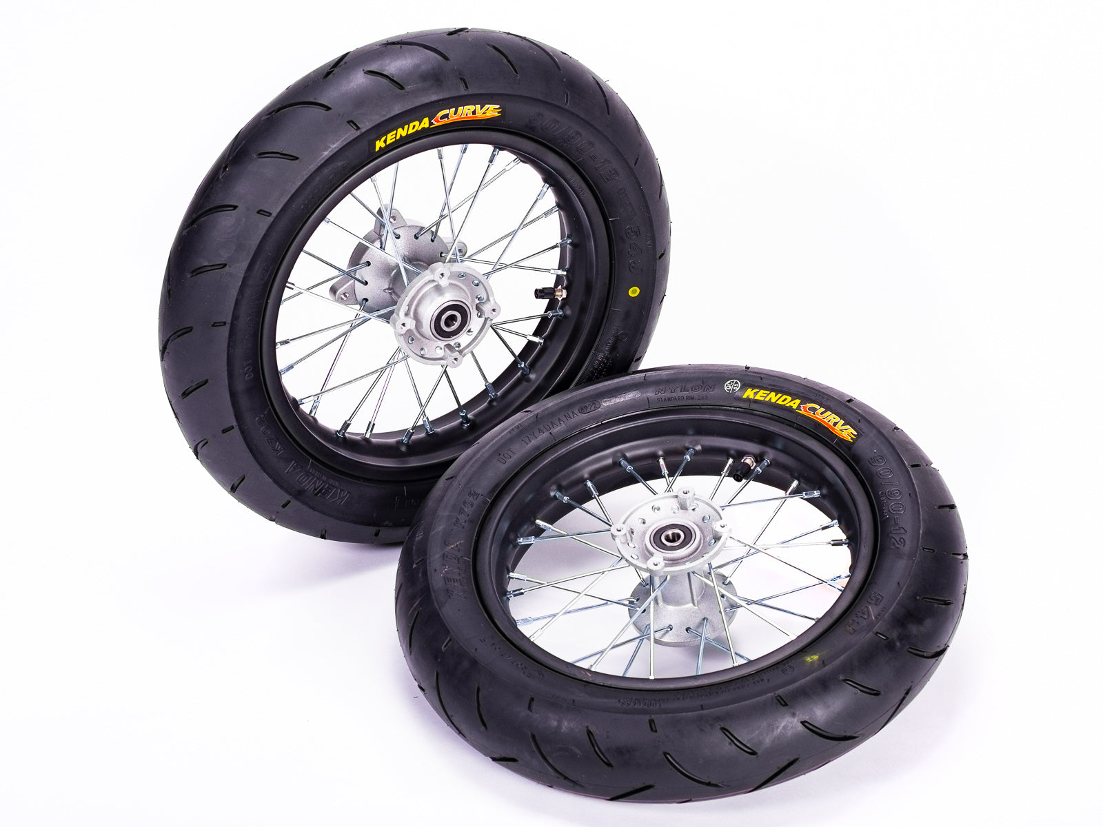 Stomp Ebox Supermoto Wheel Set 12-12, close-up view of two black alloy wheels with silver spokes and knobby tires, displayed on a white background.