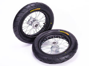 Stomp Ebox Supermoto Wheel Set 12-12, close-up view of two black alloy wheels with silver spokes and knobby tires, displayed on a white background.